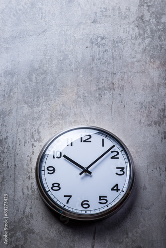 Round wall clock hanging on the grey concrete wall
