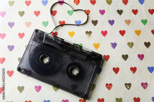 Audio cassette with magnetic tape in shape of heart on paper background