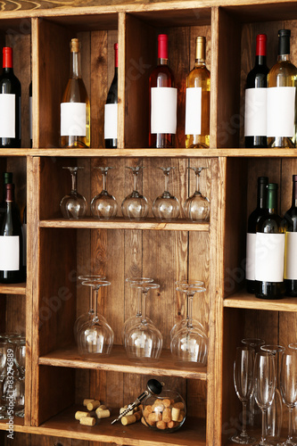 Shelving with wine bottles with glasses on wooden wall background