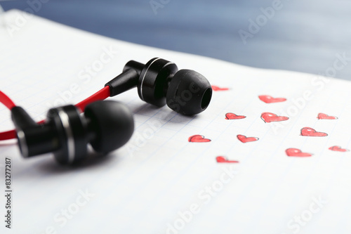 Earphones on white sheet of paper with small hearts, closeup