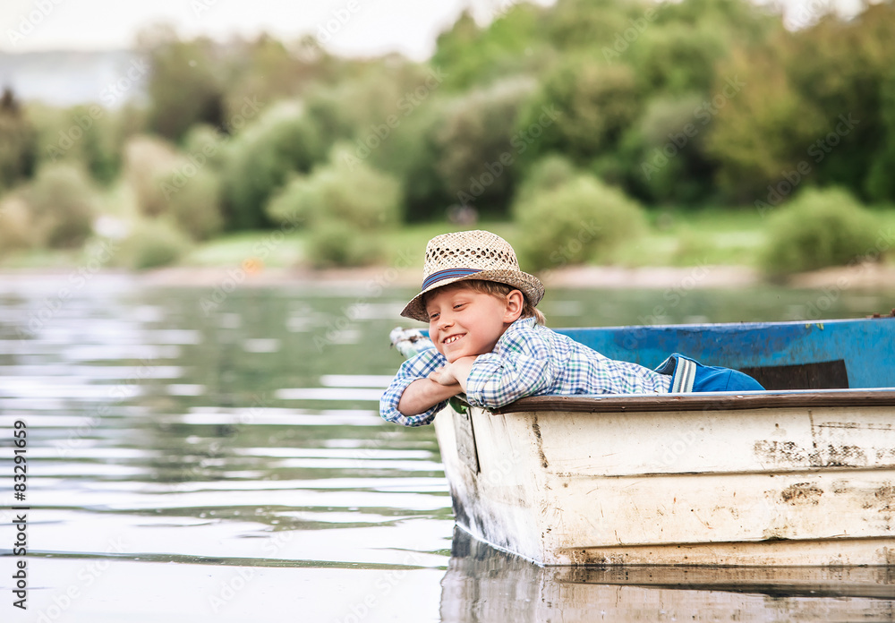 Little boy in old boat on the calm lake surface