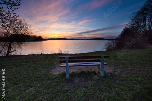 Colorful sunset over lake shore with bench