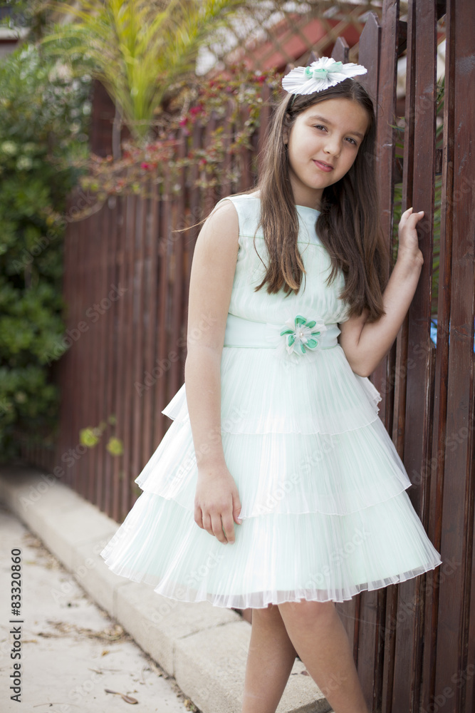 Naklejka premium Niña con vestido y tocado verde junto a valla de madera