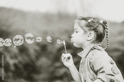 Happy little pretty girl outdoor in the park blowing bubbles