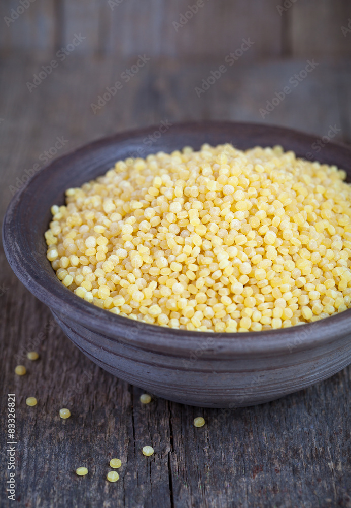 Dry Israeli couscous ptitim in a clay bowl on wooden table Dry Israeli couscous ptitim in a clay bowl on wooden table