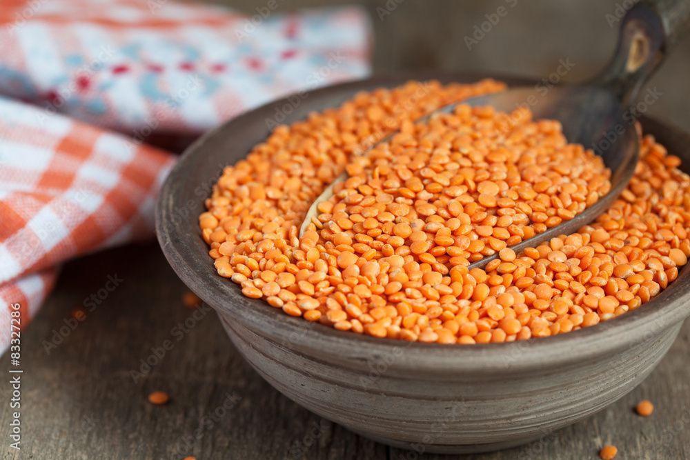 Dry red lentils in a clay bowl and in a scoop on wooden table Dry red lentils in a clay bowl and in a scoop on wooden table