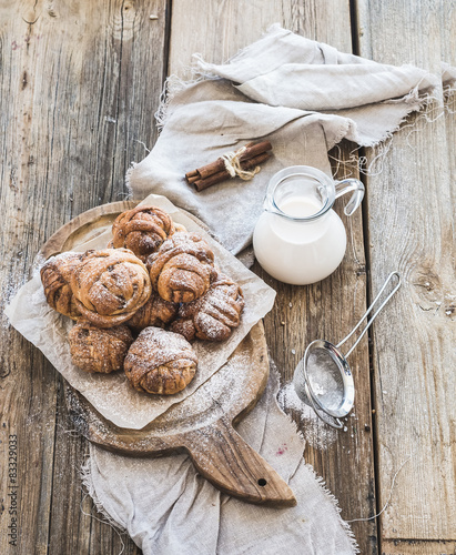 Cinnamon buns with sugar powder on rustic wooden board, jug of