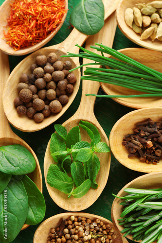 Wooden spoons with fresh herbs and spices on wooden background