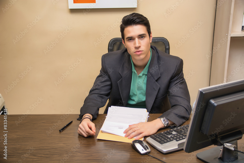 Handsome young businessman sitting at desk in office Handsome young businessman sitting at desk in office
