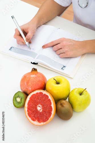 Dietician Writing Prescription With Fruits On Desk