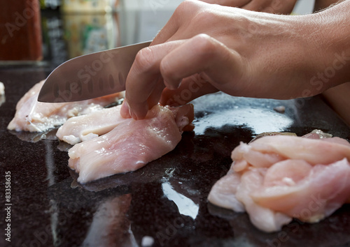 Female hands cutting raw chicken breast on black granite table