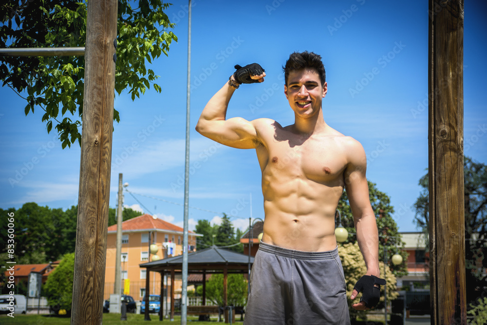 Obraz na plátně Shirtless fit athletic young man doing bicep pose outdoor