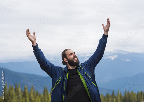 happy bearded hiker with cheering hands in mountains