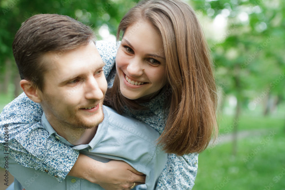 Loving couple in the park. He carries her on his shoulders Loving couple in the park. He carries her on his shoulders