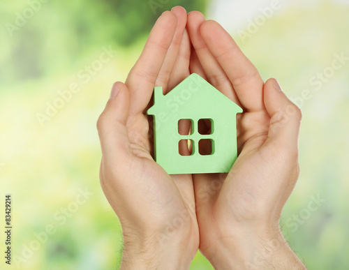 Female hands holding house on green blurred background