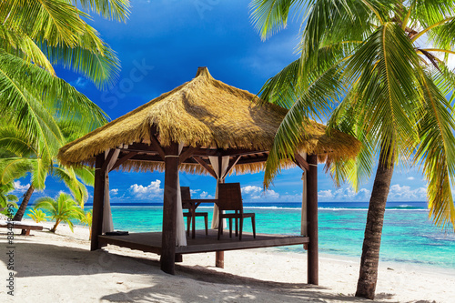 Tropical gazebo and two chairs on an island beach with palm tree