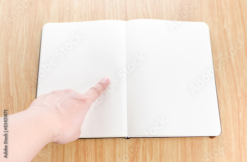 Hand pointing on blank open notebook lay it on wooden table,Temp