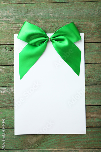 Blank paper sheet with green bow on green wooden background