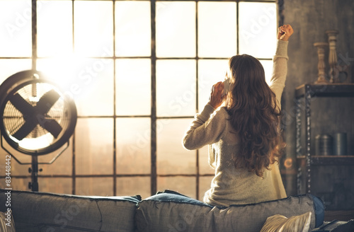 Woman seen from behind talking on phone in front of loft window photo