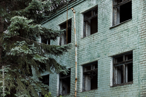 Ruined abandoned green bricks building with windows and fir tree