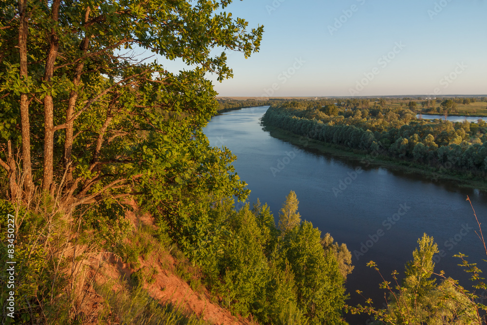 Summer landscape with a river from a high bank at sunset