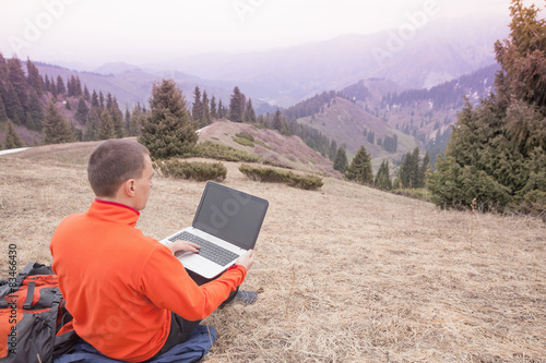 man uses laptop remotely at mountain © petunyia