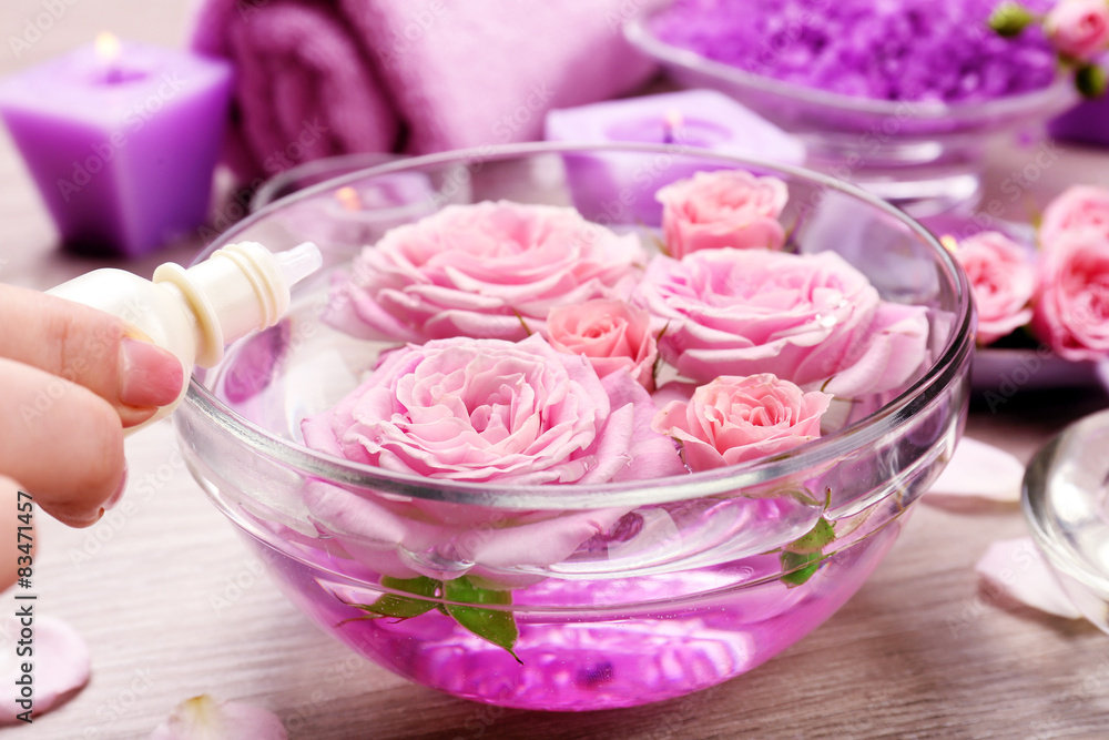 Female hand with bottle of essence and bowl of aroma spa water on wooden table, closeup Female hand with bottle of essence and bowl of aroma spa water on wooden table, closeup