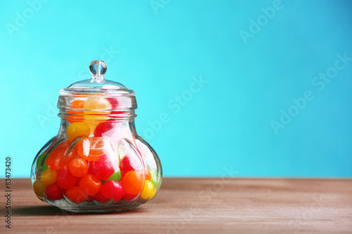 Colorful candies in jar on table on blue background