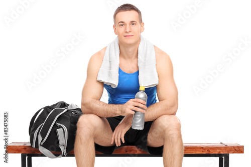 Young muscular athlete sitting on a wooden bench with a sports b