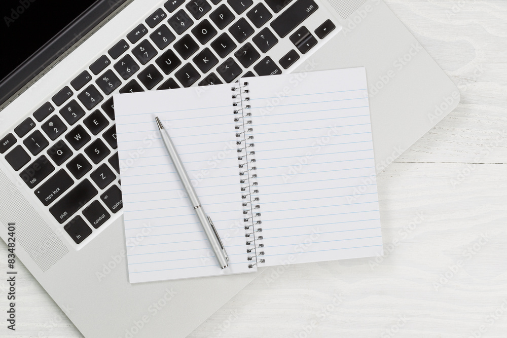 Laptop computer with blank notepad and pen on white desktop Laptop computer with blank notepad and pen on white desktop