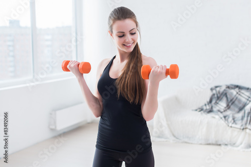 Active sportive athletic woman with dumbbells pumping up muscles