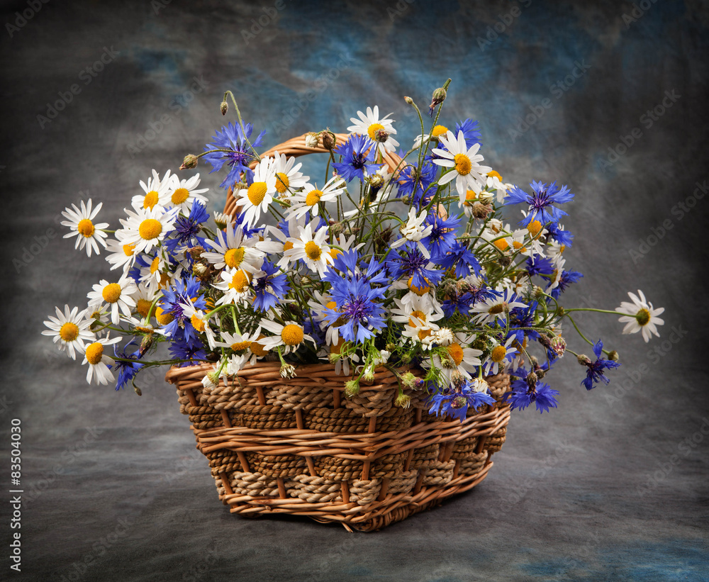 Daisies and cornflowers in a basket on table