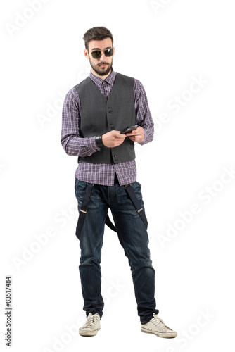 Young hipster using cell phone looking at camera
