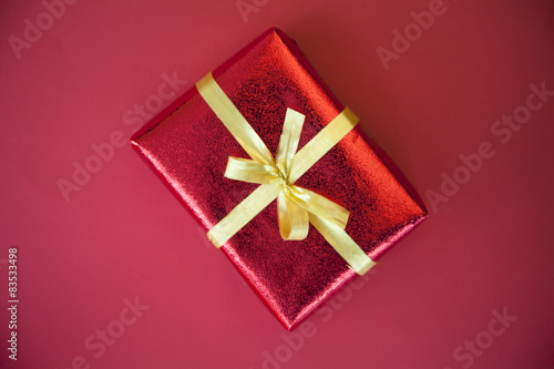 Overhead view of a red Gift box wrapped in ribbon with a gold bow on a red background 