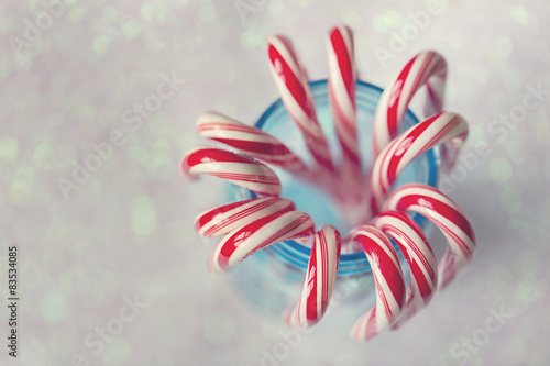 Red and white striped candy canes in blue mason jar against glittering background