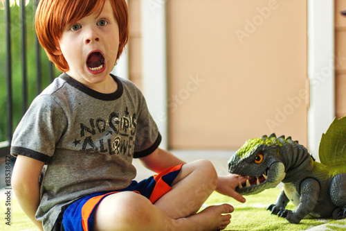 Boy sitting on the floor pretending he's screaming because he's been bitten by a toy dinosaur photo