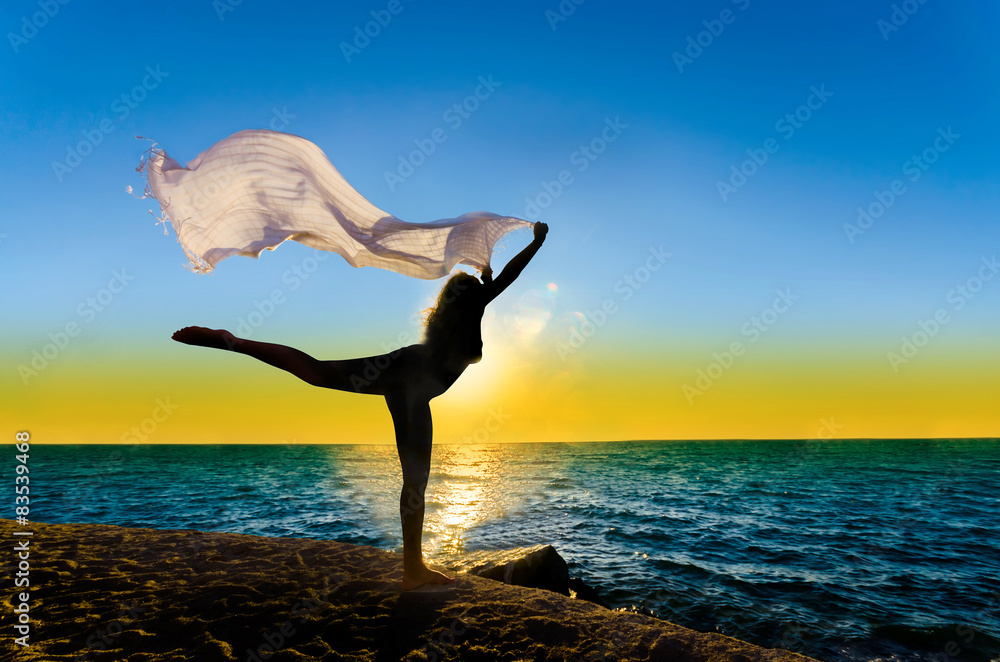 Silhouette of girl with fiber dancing at sunset sea horizon