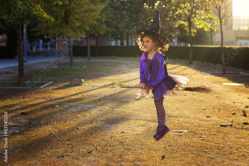 Side view of a Girl dressed as a witch flying on a broomstick in a park
