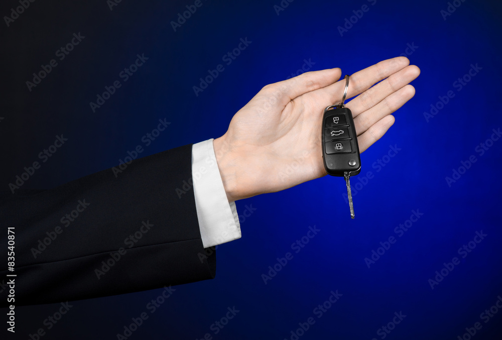 car salesman in a black suit holds the keys to a new car studio