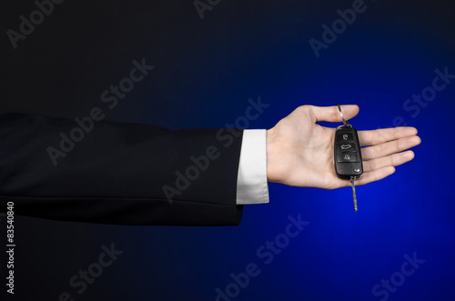 car salesman in a black suit holds the keys to a new car studio