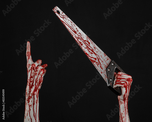 bloody hand holding a bloody saw on a black background