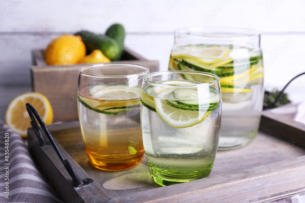 Fresh water with lemon and cucumber in glassware in wooden tray, closeup Fresh water with lemon and cucumber in glassware in wooden tray, closeup