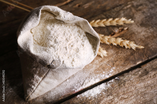 Bag of white flour with wheat ears on wooden background