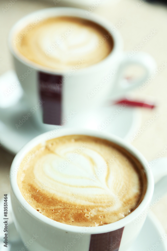 Cups of cappuccino with heart on foam on table in cafe Cups of cappuccino with heart on foam on table in cafe