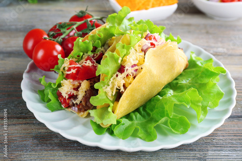 Tasty taco with vegetables on plate on table close up