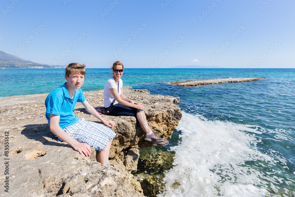 Mother and son as tourists sitting on rock at blue sea