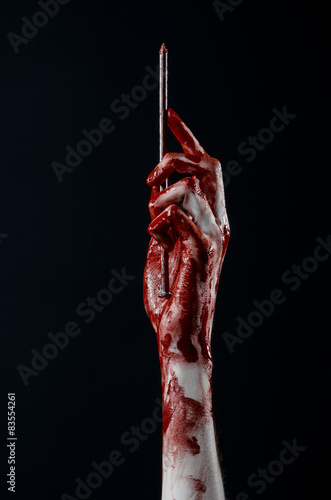bloody hand holding a large sharp nail isolated in studio