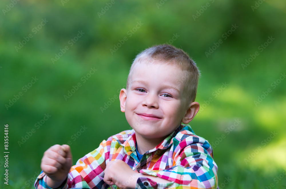 A little boy sitting on the grass and looking forward happily. A little boy sitting on the grass and looking forward happily.