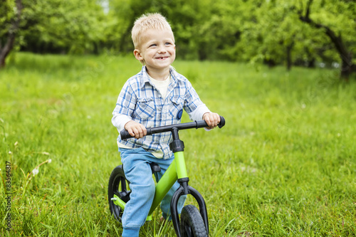 Joyful little boy riding learner bike in park 