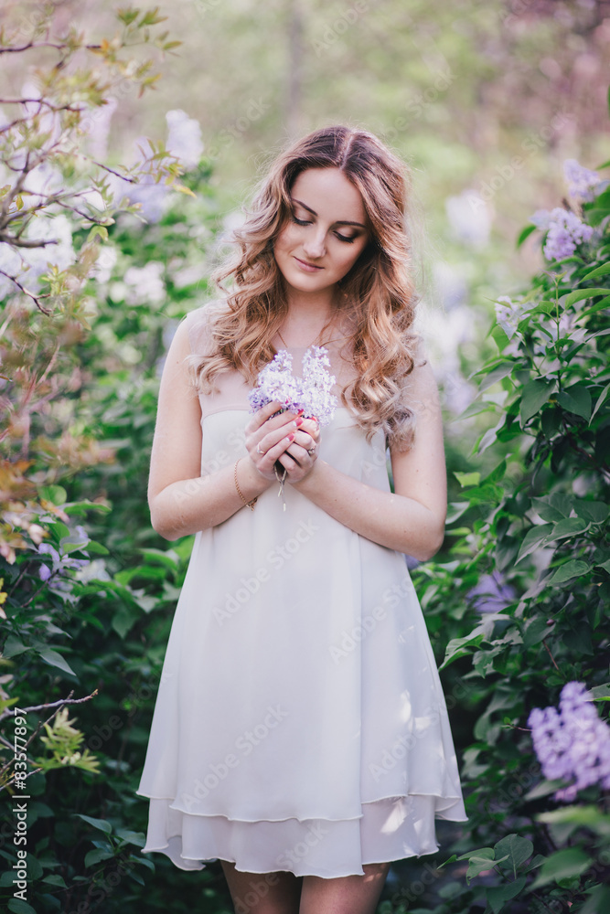Beautiful young woman with long curly hair posing with lilacs Beautiful young woman with long curly hair posing with lilacs